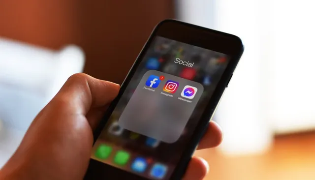 Dłoń trzymająca smartfon z folderem aplikacji społecznościowych i ikoną Instagrama — algorytm Instagrama 2026