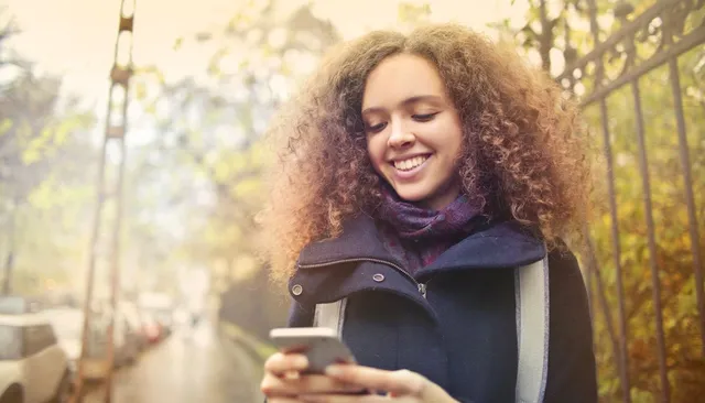 Uśmiechnięta kobieta patrzy w telefon na ulicy — jak napisać bio na Instagramie