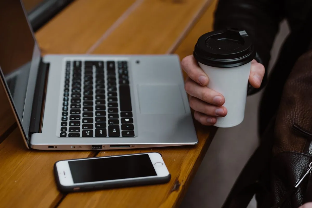 Laptop, kawa i telefon na biurku — planowanie publikacji na Instagramie